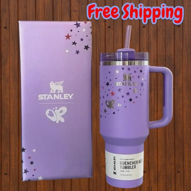 May include: A light purple Stanley Quencher H2.0 tumbler with a matching handle, lid, and straw. The tumbler features a silver star pattern and the Stanley logo. It is displayed next to a matching light purple box with the Stanley logo and stars.