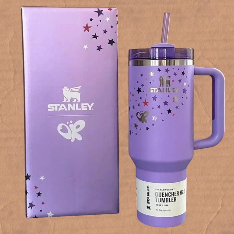 May include: A lavender Stanley Quencher H2.0 tumbler with a 1.18 L capacity, featuring a matching straw, handle, and a star-patterned design. The tumbler is accompanied by a tall, rectangular lavender box decorated with stars and the Stanley logo.