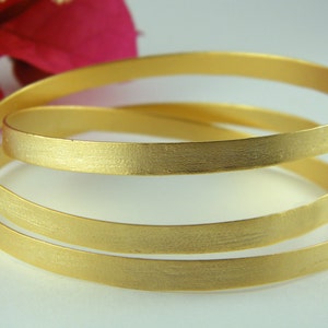 May include: Three gold-toned bangle bracelets stacked on top of each other. The bracelets have a brushed finish.
