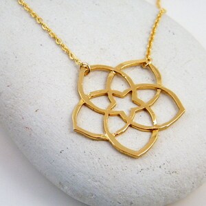 May include: Gold necklace with a geometric flower pendant. The pendant is made of a single piece of metal and has a delicate, intricate design.