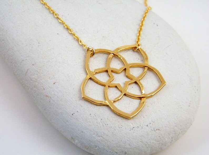 May include: Gold necklace with a geometric flower pendant. The pendant is made of a single piece of metal and has a delicate, intricate design.
