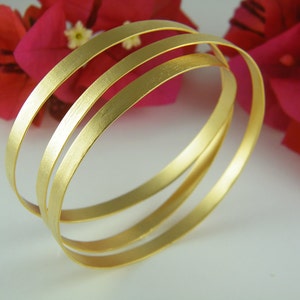 May include: Three gold-toned bangles stacked on top of each other. The bangles are smooth and have a brushed finish.