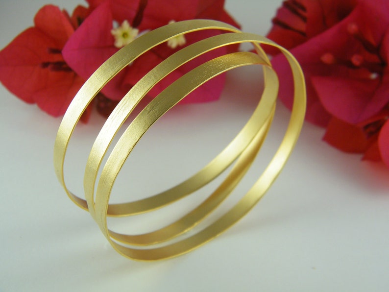May include: Three gold-toned bangles stacked on top of each other. The bangles are smooth and have a brushed finish.