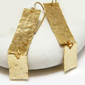 May include: Gold hammered rectangle earrings with a dangling rectangle charm. The earrings are made of brass and have a hammered texture.