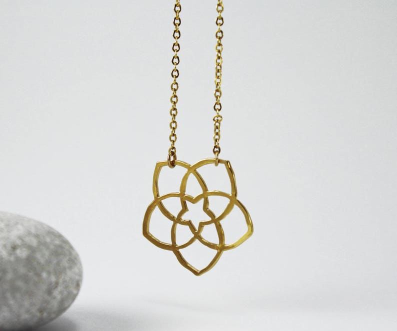 May include: Gold necklace with a geometric flower pendant. The pendant is made of a single piece of metal and has a delicate, intricate design.