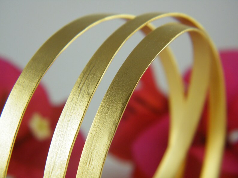 May include: Three gold-colored metal bangles stacked on top of each other. The bangles are smooth and have a brushed finish.
