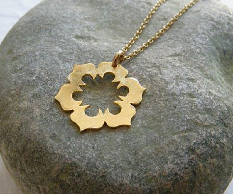 May include: A gold necklace with a delicate, openwork pendant shaped like a flower. The pendant has a circular center and eight points.