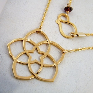 May include: A gold necklace with a delicate, intricate flower pendant. The pendant is made of a single piece of metal and features a star in the center. The necklace is attached to a chain with a lobster clasp.