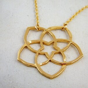 May include: A gold necklace with a delicate, geometric pendant in the shape of a flower. The pendant is made of interlocking circles and has a star-shaped center.