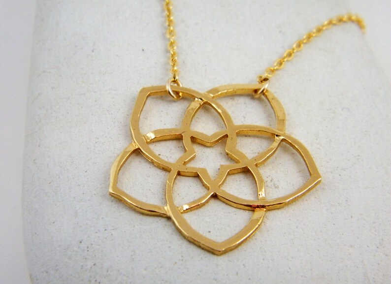 May include: A gold necklace with a delicate, geometric pendant in the shape of a flower. The pendant is made of interlocking circles and has a star-shaped center.