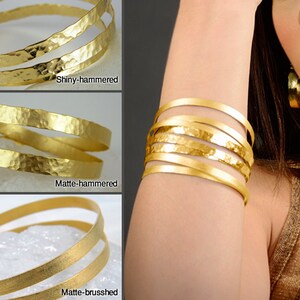 May include: Three gold bracelets with different finishes: shiny-hammered, matte-hammered, and matte-brushed. The bracelets are stacked on top of each other.
