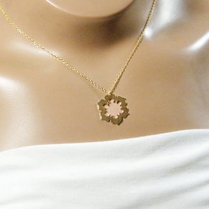 May include: A gold chain necklace with a delicate pink flower pendant. The pendant has a cutout design and a smooth, polished finish.