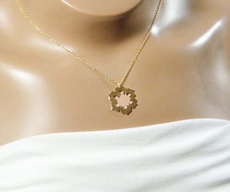 May include: A gold chain necklace with a delicate pink flower pendant. The pendant has a cutout design and a smooth, polished finish.