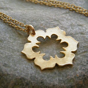 May include: A gold necklace with a delicate, openwork pendant in the shape of a flower. The pendant has a circular center and eight petals with intricate cutouts.