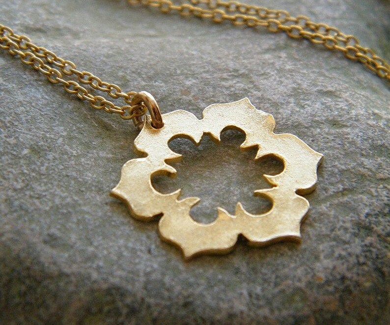 May include: A gold necklace with a delicate, openwork pendant in the shape of a flower. The pendant has a circular center and eight petals with intricate cutouts.