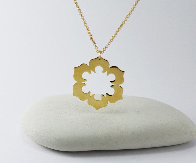 May include: A gold necklace with a large, openwork pendant in the shape of a flower. The pendant is made of a single piece of metal and has a delicate, intricate design.