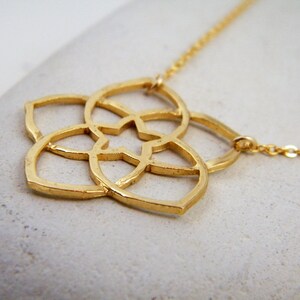 May include: A gold necklace with a delicate, geometric flower pendant. The pendant is made of thin metal and has a detailed, intricate design.