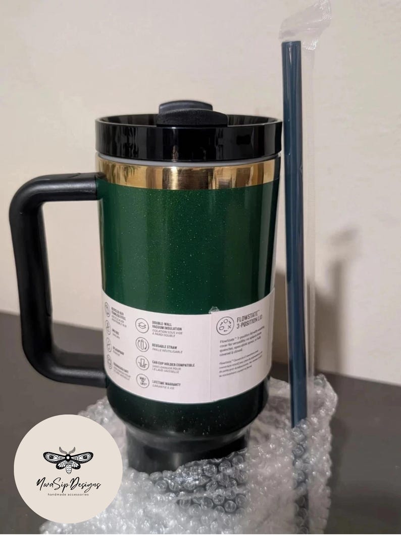 May include: Green travel mug with a black handle and lid, accented with gold trim. Includes a reusable straw. Features double-wall vacuum insulation and a lifetime warranty. The mug is designed for hot and cold beverages.