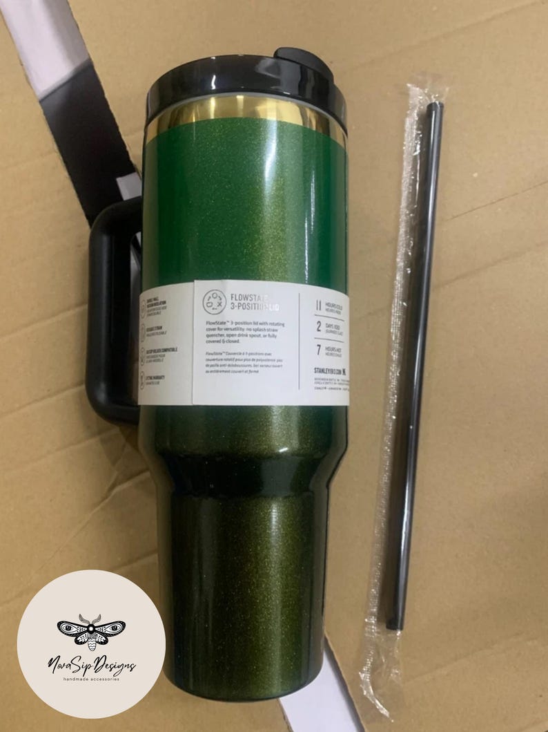 May include: A green glitter travel tumbler with a black handle and lid. The tumbler has a gold band near the top and a white label with text. A black straw is included. The tumbler is designed for hot and cold beverages.