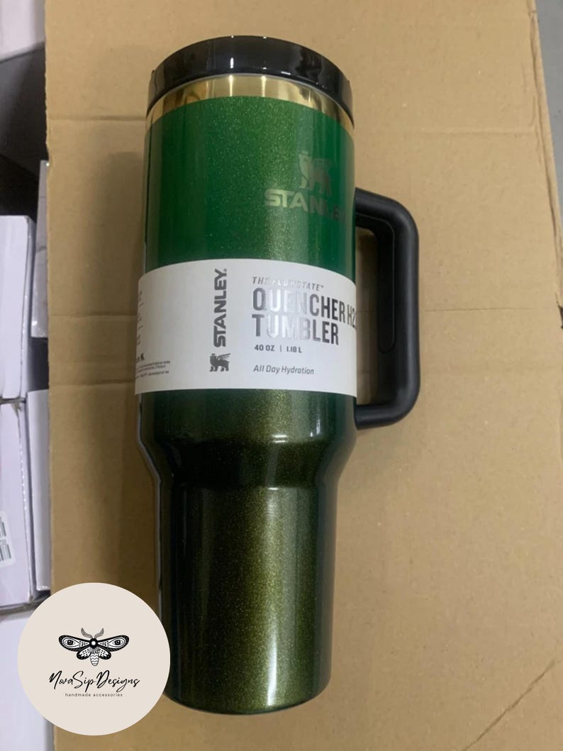 May include: A green Stanley Quencher H2.0 tumbler with a black handle and lid. The tumbler has the Stanley logo and text that reads "QUENCHER TUMBLER 40 OZ | 1.1L All Day Hydration". The tumbler is designed for all-day hydration.