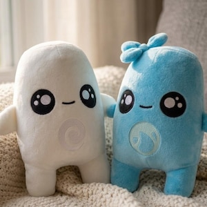 May include: Two plush toys with rounded bodies and short limbs. The left toy is white with a spiral emblem on its chest. The right toy is light blue with a bow on top and a water drop emblem on its chest. Both have large black eyes with white highlights.