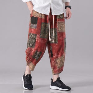 Puede incluir: Pantalones cortos rojos estampados con cintura con cordón. El diseño de patchwork presenta patrones en tonos marrones, verdes y negros. La persona lleva zapatillas negras y una camisa blanca abotonada. Los pantalones miden unos 76 cm de largo.