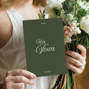 Op de afbeelding: Een donkergroene kaart met de woorden "Her Vows" in elegant wit schrift. De kaart wordt voor een boeket witte en groene bloemen gehouden. De datum "10.10.26" staat bovenaan gedrukt.