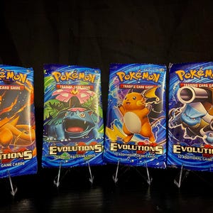 May include: Four Pokémon Trading Card Game booster packs. Each pack features a different Pokémon character: Charizard, Venusaur, Pikachu, and Blastoise. The packs are blue with the word "EVOLUTIONS" and "10 ADDITIONAL GAME CARDS" printed on them.