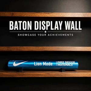 Może przedstawiać: Niebieska metalowa pałeczka sztafetowa spoczywająca na drewnianej półce. Pałeczka posiada białe logo Nike, napis Lion Mode oraz napis 2015 NIKE INDOOR NATIONALS. Nad półką widnieje napis BATON DISPLAY WALL SHOWCASE YOUR ACHIEVEMENTS.