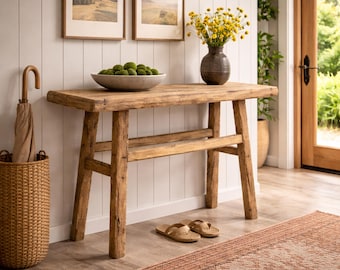 Op de afbeelding: Een rechthoekige houten sidetable met vier poten en een onderste plank. Bovenop staat een grijze schaal gevuld met groene mosballen en een donkere keramische vaas met gele bloemen. Een beige paraplu staat in een gevlochten mand ernaast.
