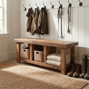 May include: A rectangular wooden entryway bench with a natural finish, featuring three open storage compartments. Two compartments contain woven seagrass baskets, while the third holds folded cream-colored knit blankets.