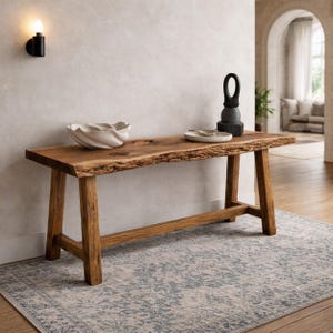 Peut inclure: Une console en bois rustique avec un dessus à bord brut et des pieds inclinés. La table est ornée d'un bol en céramique blanc, d'une petite assiette et d'une sculpture noire. Elle repose sur un tapis à motifs.