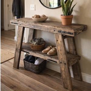 May include: A distressed wooden console table with a lower shelf and angled legs. The table is made of reclaimed wood and features metal accents. A woven basket, shoes, and decorative items are displayed on the shelves.