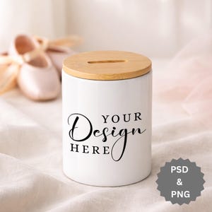 Op de afbeelding: Witte keramische pot met een natuurlijk houten deksel. Op de pot staat in zwart schrift "YOUR Design HERE". Een paar balletschoentjes zijn wazig op de achtergrond. De pot heeft een cilindrische vorm.