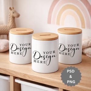 Könnte beinhalten: Drei weiße Keramikbehälter mit Holzdeckeln stehen auf einem Holzregal. Auf jedem Behälter steht in schwarzer Schrift "YOUR Design HERE". Die zylindrischen Behälter haben einen Schlitz im Deckel. Die Behälter sind ca. 15 cm hoch.
