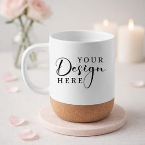 Puede incluir: Taza de cerámica blanca con base de corcho, con el texto "YOUR Design HERE" en escritura negra. La taza está sobre un posavasos rosa, con pétalos de flores rosas esparcidos. Dos velas encendidas y un jarrón con flores rosas en el fondo.