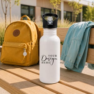 Puede incluir: Una botella de agua de metal blanco con una tapa de rosca negra y un asa de transporte. La parte frontal de la botella presenta el texto impreso en negro "YOUR DESIGN HERE" en una combinación de fuentes serif y script, centrado en la superficie.