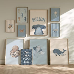 May include: A gallery wall set of ten framed prints featuring illustrations of sea creatures including a hammerhead shark with the name HUDSON, an octopus, a whale, a crab, a turtle, a jellyfish, and a sign reading STAY WILD OCEAN CHILD.