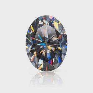 Puede incluir: Una piedra preciosa de corte ovalado con un color de cuerpo gris oscuro y una superficie facetada que muestra intensos reflejos de luz de colores del arcoíris. La piedra presenta una disposición simétrica de facetas que crean un patrón estelar.