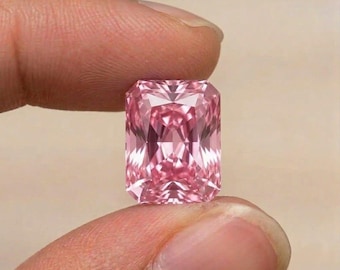 Puede incluir: Una piedra preciosa de corte radiante con un tono rosa vibrante y una superficie facetada que refleja la luz. La piedra presenta una forma rectangular con esquinas recortadas, mostrando una calidad clara, transparente y facetas simétricas.