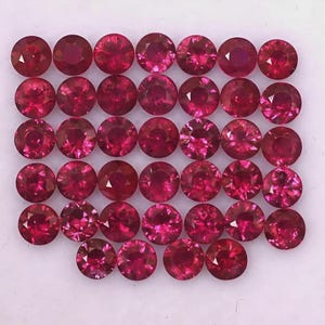 May include: A collection of thirty-four round, faceted, vibrant red gemstones arranged in a grid pattern. Each stone features a brilliant cut with multiple facets that reflect light, creating a consistent deep crimson color across the entire set.