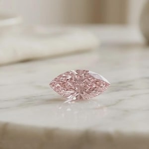 Può includere: Una pietra preziosa taglio marquise con una tonalità rosa chiaro e una superficie sfaccettata. La pietra presenta una forma ovale appuntita con sfaccettature simmetriche che riflettono la luce, creando un aspetto brillante su tutto il corpo rosa.