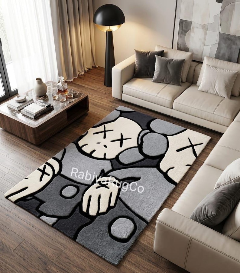 May include: A rectangular area rug featuring a stylized character design with X-shaped eyes in shades of cream, light gray, and dark charcoal gray. The rug displays the text "RabiyaRugCo" in white lettering across the center of the graphic pattern.