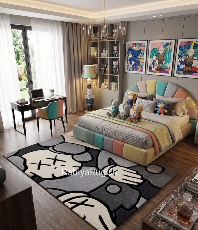 May include: A bedroom featuring a large area rug with a gray, black, and white cartoon character graphic and the text "RabiyaRugCo". The room includes a bed with a multi-colored headboard, several plush toys, a desk, a chair, and wall art.