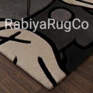 May include: A tufted area rug featuring a graphic design in cream, dark gray, and black. The rug displays bold black outlines and the text "RabiyaRugCo" printed in white across the center. The surface has a thick, textured pile construction.