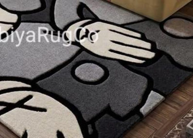 May include: A rectangular area rug featuring a stylized graphic design in shades of black, dark gray, and light gray. The pattern includes large, rounded shapes and hand-like forms outlined in thick black lines. The text biyaRugCo is visible.