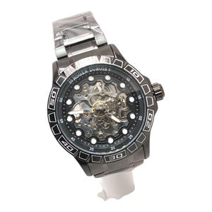 Può includere: Un orologio Roger Dubuis nero con quadrante scheletrato, che mostra i meccanismi interni. L'orologio ha una lunetta nera con numeri bianchi e un cinturino in metallo nero. È un accessorio elegante.