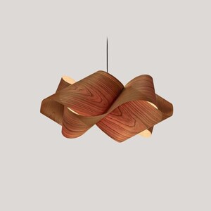 May include: A modern, sculptural pendant light fixture. The light features a unique design with layered, curved wooden panels, showcasing a natural wood grain pattern. The fixture hangs from a black cord, creating a warm, ambient glow.