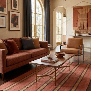 May include: A rectangular area rug featuring a terracotta orange base with horizontal stripes in dark brown and tan. The rug is positioned in a living room setting with a wooden coffee table, a rust-colored sofa, and a leather armchair.