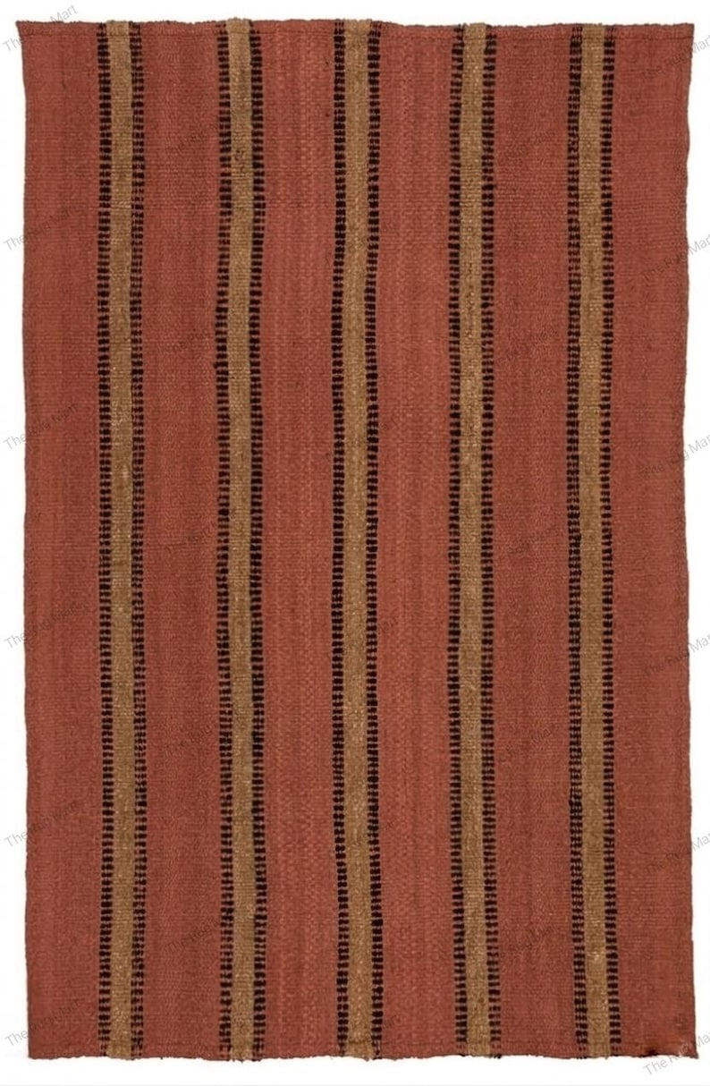 May include: A rectangular woven rug featuring a solid terracotta red base color. The rug is decorated with a repeating pattern of vertical stripes in alternating shades of dark brown and tan, creating a textured and linear visual appearance.